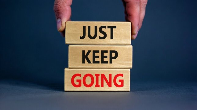 Hand placing wooden blocks with motivational phrase 'Just Keep Going' for perseverance and resilience concept