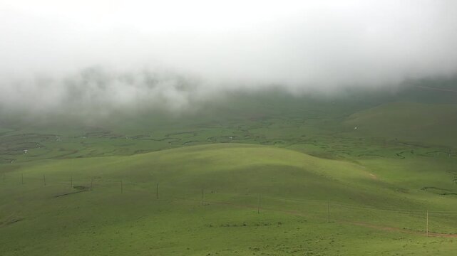 Time lapse clouds drift above treeless hill grasslands covered with vivid green summer growth.