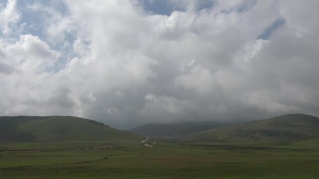Time lapse clouds drift above treeless hill grasslands covered with vivid green summer growth.