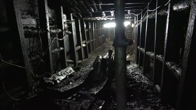 Dark wet underground mine tunnel corridor with timber supports and muddy ground texture.