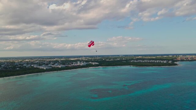 Aerial view of parasailing over the blue turquoise sea in Playa del Carmen. Drone shot of red parasail glidder soaring over Caribbean ocean in Riviera Maya, Mexico.