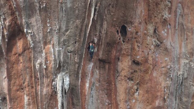 Sporty mountaineer climbing a high flat rock wall on a rugged mountain cliff face.