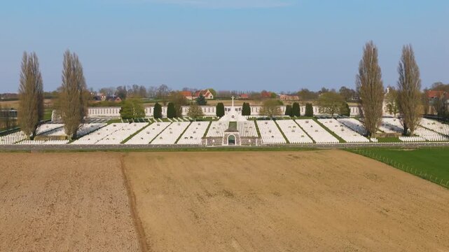 wwi cemetery tyne cot aerial cinematic view vast white headstone expanse between tall poplar trees curved memorial wall farmland zonnebeke belgium flanders remembrance lest we forget armistice 1917