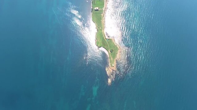 Panoramic aerial view of elongated promontory peninsula extending into blue sea at sunrise.