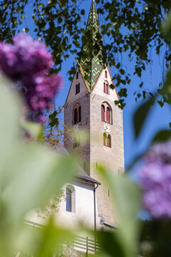 Eine Kirche im Allg&auml;u umringt von unscharfen Bl&auml;ttern und Bl&uuml;ten 