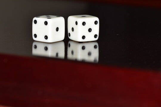 A pair of white, six-sided dice resting on a glossy black surface with a clear reflection, displaying a total sum of seven (a four on the left die and a three on the right die)