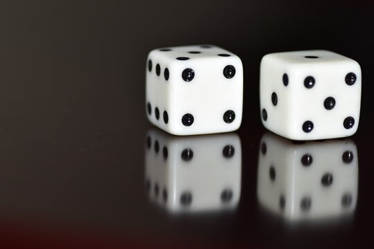 A pair of white, six-sided dice resting on a glossy black surface with a clear reflection, displaying a total sum of seven (a four on the left die and a three on the right die)