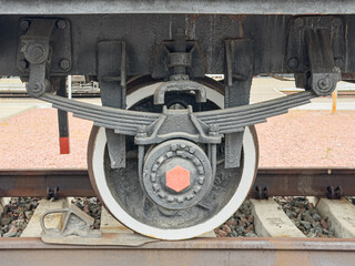 Close-up railway wheelset with detailed mechanics, intricate components including wheel, axle, brake mechanism, gear teeth, bolts and nuts, wear patterns, set against a railway yard background © Mister