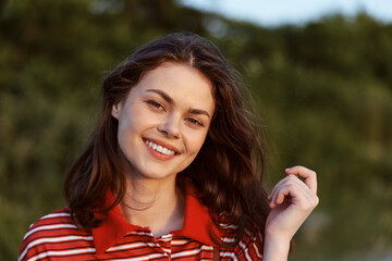 Obraz premium Smiling woman lifestyle portrait outdoor. Young lady with natural make up wearing casual shirt. Sunny summer day light creates a joyful happy mood for this lifestyle concept.