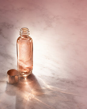 Open glass bottle with liquid and cap on marble surface with soft light and shadow nad plus warm elegant atmosphere