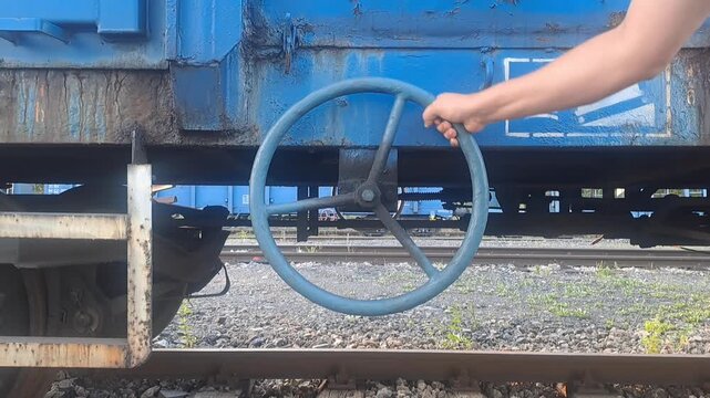 Hand operating brake wheel on blue freight railway wagon.