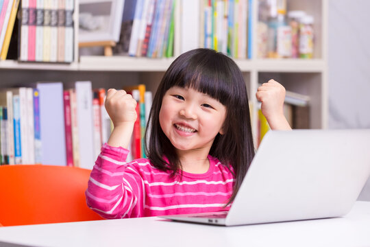 Confident Asian Child Girl Raising Fists Celebrating Success in Online Learning