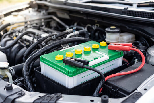 Car battery with a vibrant green top and attached red and black jumper cables in an engine bay