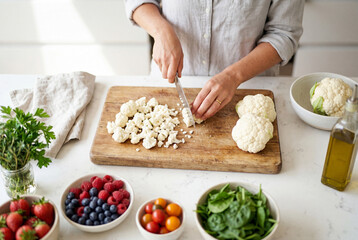 Fototapeta premium Woman cutting fresh white cauliflower on a wooden board