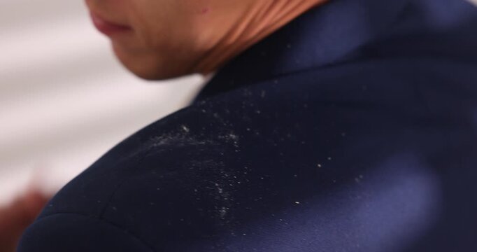Young man brushing dandruff off his suit against blurred grey background, closeup. Camera moving forward