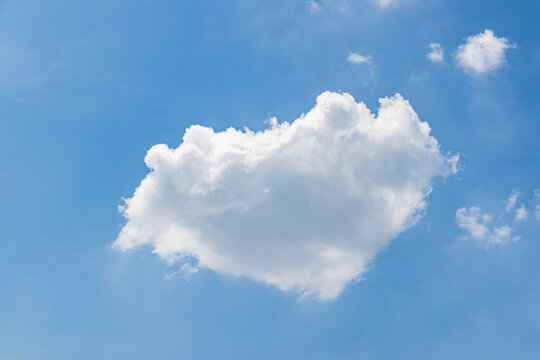 Bright blue sky with a large fluffy white cumulus cloud and small scattered clouds, clear and serene daytime scene.