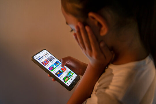 Riau, July 18, 2025, Close-up of a child's hands holding a smartphone, playing a colorful 3D Roblox obby game in a dimly lit room, highlighting youth gaming and screen time habits.