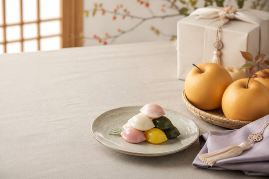 Korean harvest table setting with songpyeon, ripe pears, hanbok fabric napkin, and gift box, Chuseok celebration concept