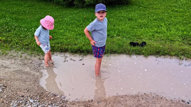 Boy and girl having fun together splashing and stomping in a big mud puddle in a park