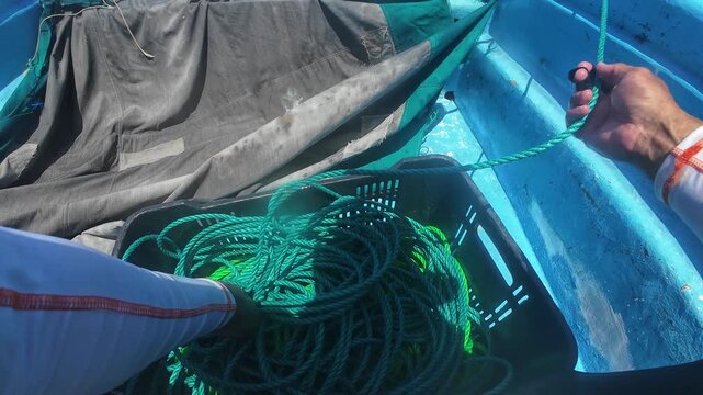 POV man pulling anchor line, rope used to hold and retrieve the anchor or grapnel of fishing boat while choppy ocean water surrounds the vessel.