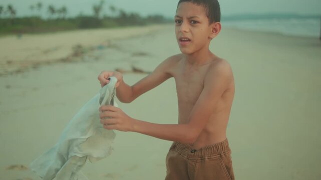 Close-up of a boy on the beach trying to put on his t-shirt in the wind