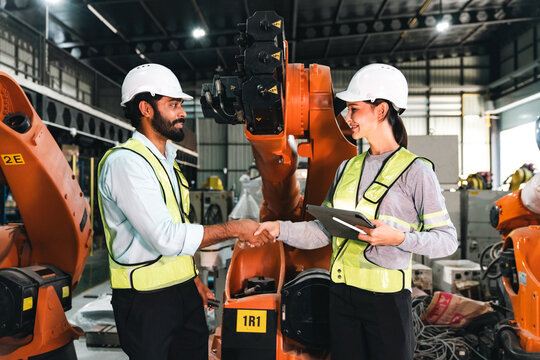 Engineer worker handshake robot factory safety helmet vest teamwork industry male and female engineer shaking hand near industrial robot factory, wearing safety helmet and reflective vest