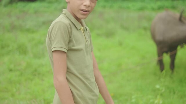Boy standing in grassy field with buffalo in background, rural outdoor setting