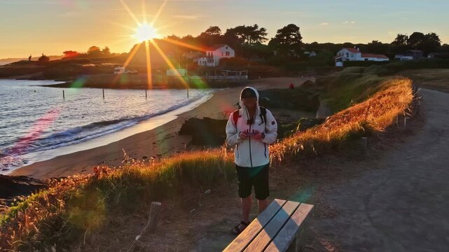 Camera pulls out from drone operator on coastal path revealing sunrise beach cove and seaside houses near Nantes France
