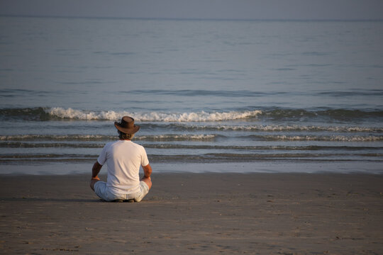 Man meditating on quiet beach facing the ocean