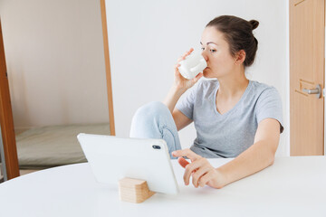 Woman drinking coffee while browsing on a tablet at home. Using touchscreen technology, internet browsing, digital device and everyday online activity. © soya