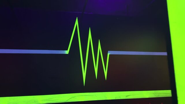 A close-up shot of a glowing neon green heartbeat pulse painted on a dark wall. The vibrant ultraviolet graphic features blue and red accents, illuminated by blacklight inside an entertainment center.