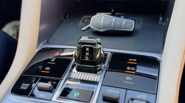 A close-up static shot of a modern luxury car center console during daylight. The interior features a crystal gear shifter, electronic control buttons, and a smart key fob resting on a charging pad.