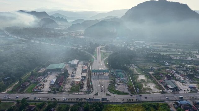 Misty mountains loom over winding highway. Vehicles move slowly through checkpoint zone at Simapng Pulai, Perak
