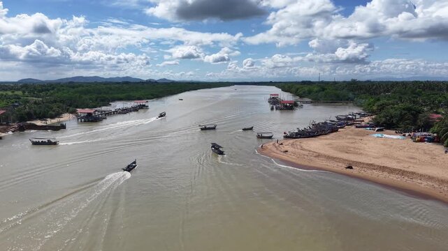 Boats glide across wide, muddy river under cloudy sky at Kuala Muda, Penang