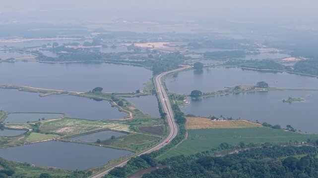 Ground level view of abandoned tin mining lakes with winding road and empty levees under hazy sky at Kampar, Perak