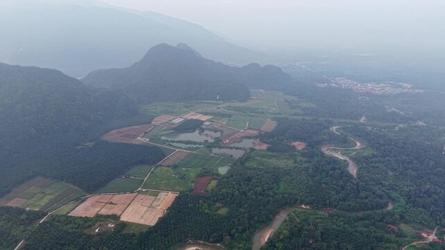 Aerial view shows mountains and farmland. Winding road cuts through green fields at Kampar, Perak