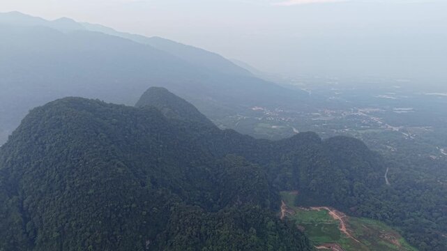 Aerial drone captures lush green mountain peaks. Misty valleys stretch to distant town at Kampar, Perak