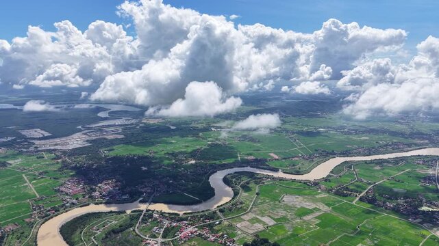 Aerial view of winding river through lush green fields. Massive clouds drift above the landscape at Kuala Muda, Penang
