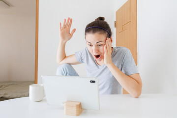 Surprised woman using tablet at home, shocked by unexpected news or information on screen, emotional reaction to online content. © soya