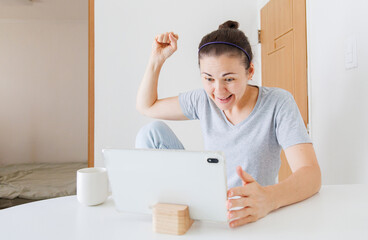 Excited woman looking at tablet at home, happy about good news, successful result, achievement and positive online information. © soya