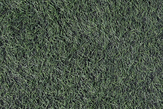 Full frame texture of synthetic grass on a soccer field, realistic artificial turf with subtle black rubber granules from top view
