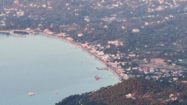 Scenic drone flight over Ipsos (Ypsos) beach in Corfu, Greece. The aerial footage shows the long coastline of the tourist resort with calm Ionian sea waters, sandy shore, and lush green hills.