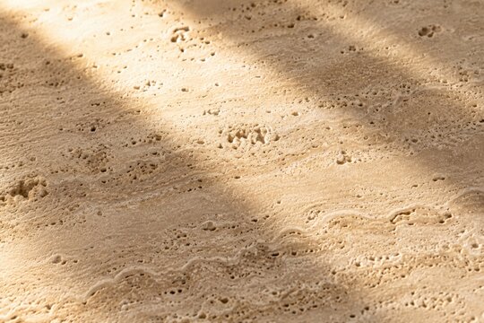 Sunlight and shadow patterns on soft beige sand surface texture