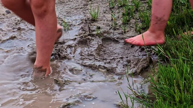 Two children joyfully playing and stomping barefoot in a thick, wet mud puddle on a grassy field