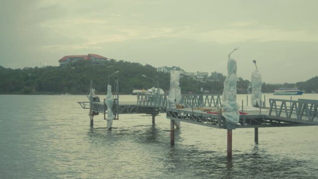 Small riverside pier with floating docks extending into calm water under an overcast sky. Ideal for travel, waterfront, transportation, marina, and tourism projects. Kala Academy Jetty in Panaji, Goa