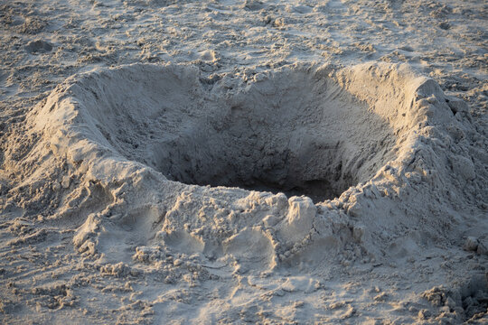 Large rectangular hole dug in beach sand with footprints around it