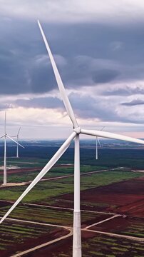 Close aerial view of wind turbine above agricultural fields, vertical ascend