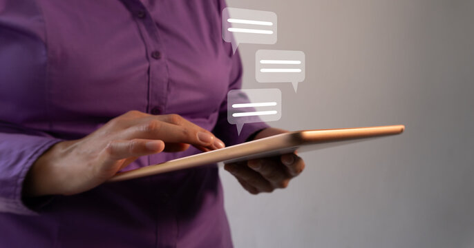 Woman holds tablet. Fingers tap screen with focus and intent. Three floating speech bubbles hover nearby. Digital interaction feels modern and seamless