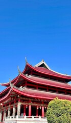 Fototapeta premium Low angle view of red Chinese lanterns hanging under the traditional curved roof of a temple against a bright blue sky.