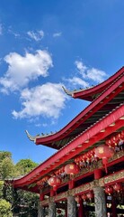 Obraz premium Low angle view of a magnificent multi tiered red Chinese temple building with traditional carved pillars against a vibrant blue sky.